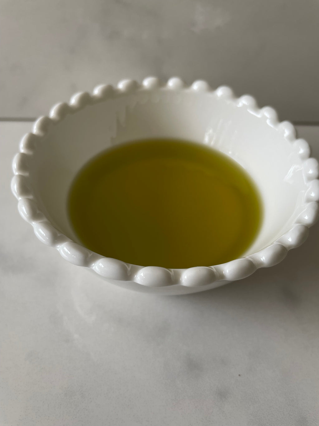 Greek Earth Extra Virgin Olive Oil poured into a white ceramic bowl